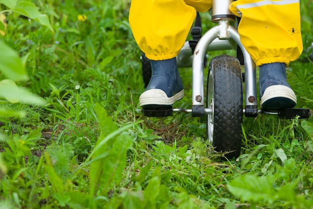 Maluch stopy dziecka w kaloszach i spodniach jadący na rowerze po zielonej trawie Chłopiec spacerujący na świeżym powietrzu