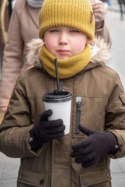 Mały 5-letni chłopiec trzymający kubek z rozgrzewającym napojem na zewnątrz