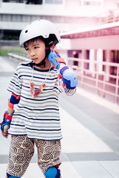 Mały azjatycki chłopiec uczy się jeździć na rolkach w parku z pełnym ochraniaczem i kaskiem