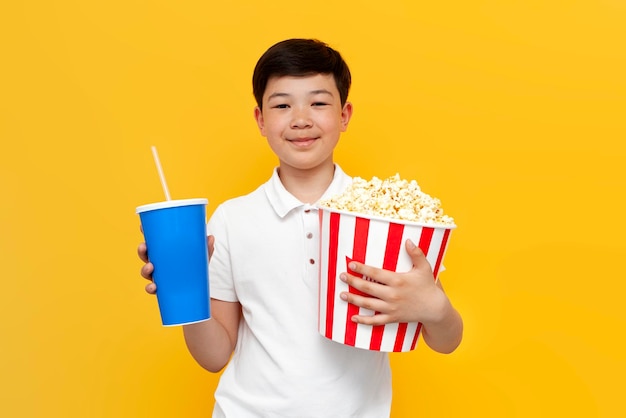 mały azjatycki chłopiec z popcornem i napojem gazowanym uśmiecha się na żółtym tle Koreańska przeglądarka dziecięca