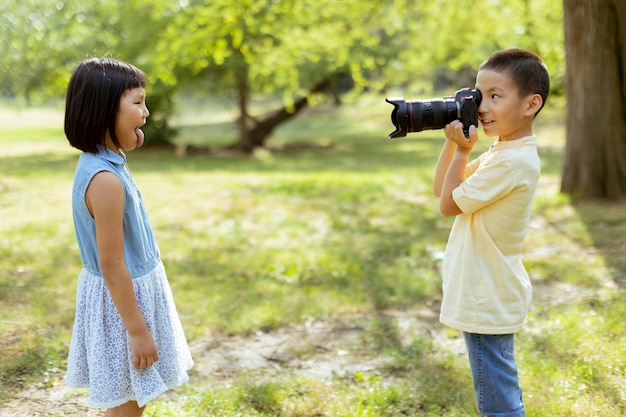 Mały azjatycki chłopiec zachowujący się jak profesjonalny fotograf podczas robienia zdjęć swojej młodszej siostrze