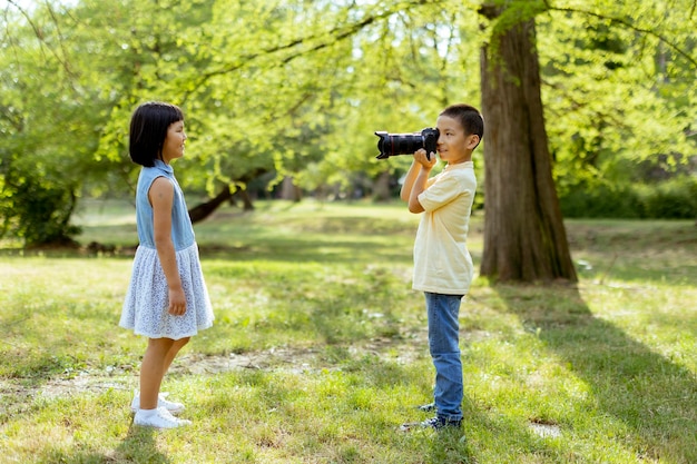 Mały azjatycki chłopiec zachowujący się jak profesjonalny fotograf podczas robienia zdjęć swojej młodszej siostrze