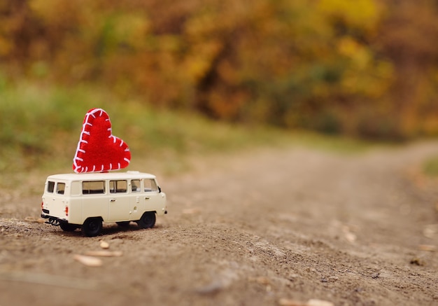 Mały biały minivan samochodzik jedzie na dachu wielkiego czerwonego serca