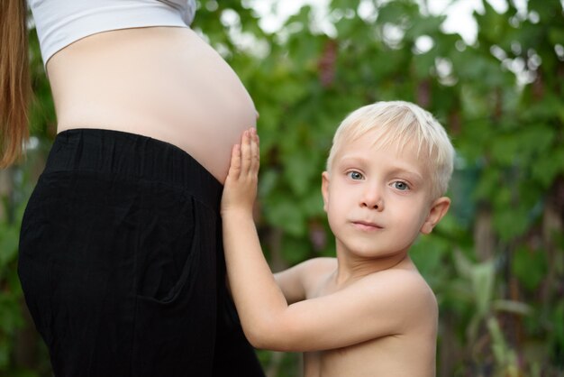Zdjęcie mały blond chłopiec głaszcze brzuch swojej ciężarnej matki. koncepcja rodziny