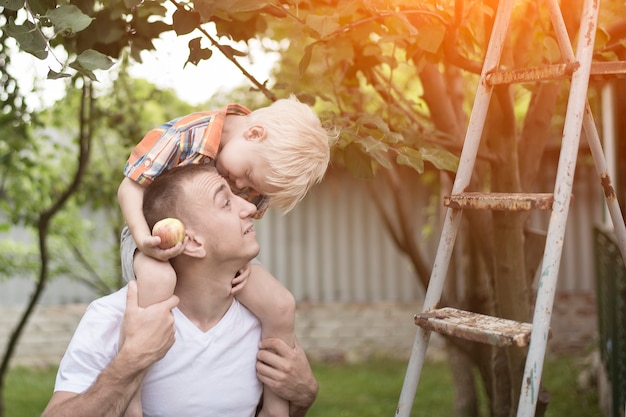 Mały blond chłopiec z jabłkiem w rękach na ramionach ojca.