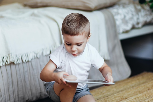 Zdjęcie mały chłopiec bawi się na tablecie w pokoju dziecięcym jasne wnętrze