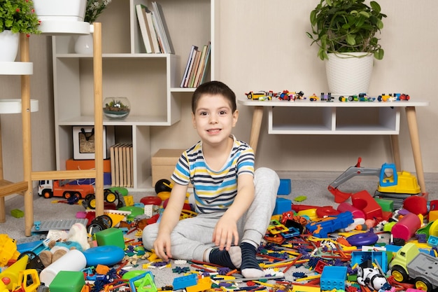 Mały chłopiec bawiący się zabawkami siedzący na podłodze wśród rozrzuconych zabawek bałagan w pokoju dziecięcym