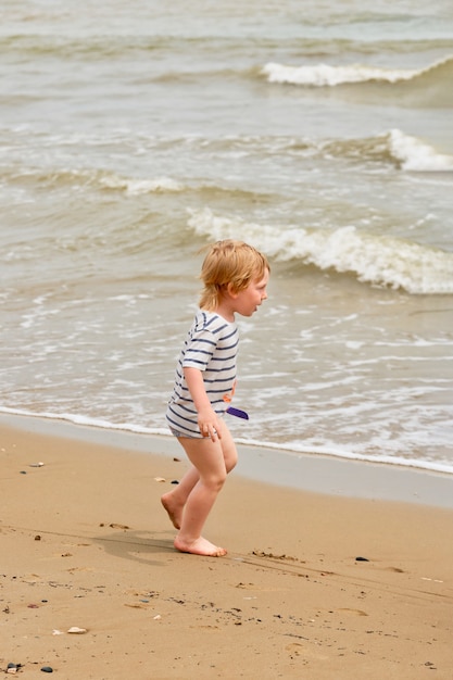 Mały chłopiec biegnie wzdłuż piaszczystej plaży nad brzegiem morza. Dziecko odpoczywające na morzu