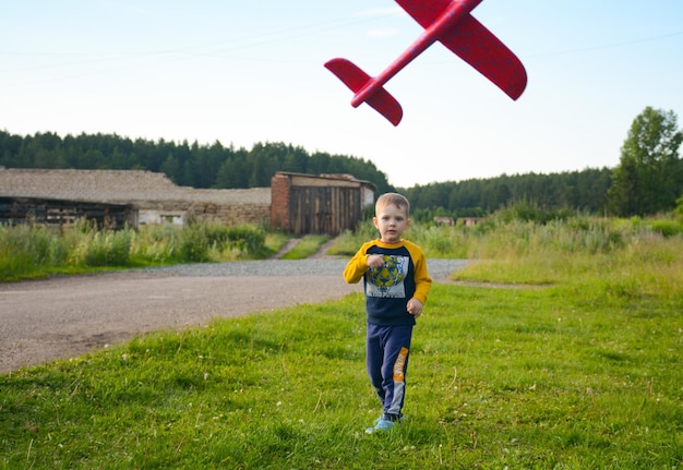 Mały chłopiec, dzieciak na ulicy bawiący się zabawką z czerwonym samolotem.