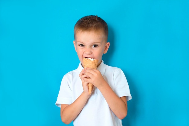 Mały chłopiec je lody w rożku na niebieskim tle z wolnym miejscem do kopiowania tekstu