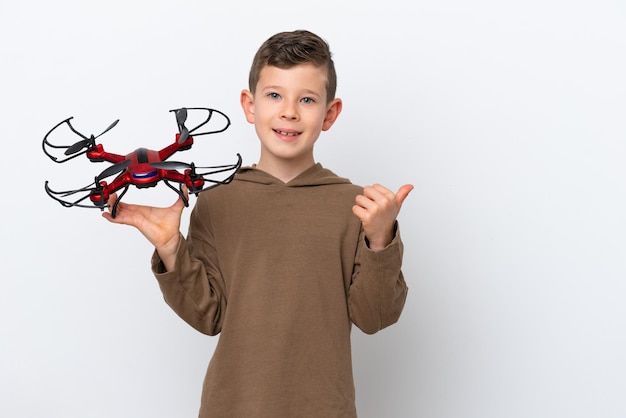Mały chłopiec kaukaski trzymający drona na białym tle wskazujący na bok, aby zaprezentować produkt