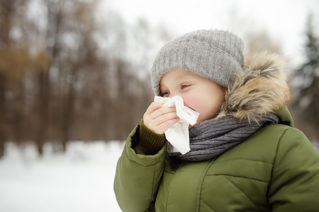 Mały Chłopiec Kichanie I Wyciera Nos Serwetką Podczas Spaceru W Winter Park. Sezon Grypowy I Przeziębienie Nieżytu Nosa. Alergiczny Dzieciak.