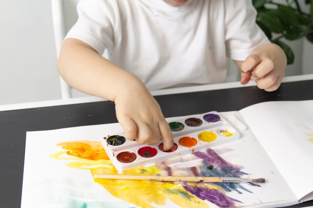 Mały chłopiec maluje farbami akwarelowymi na stole