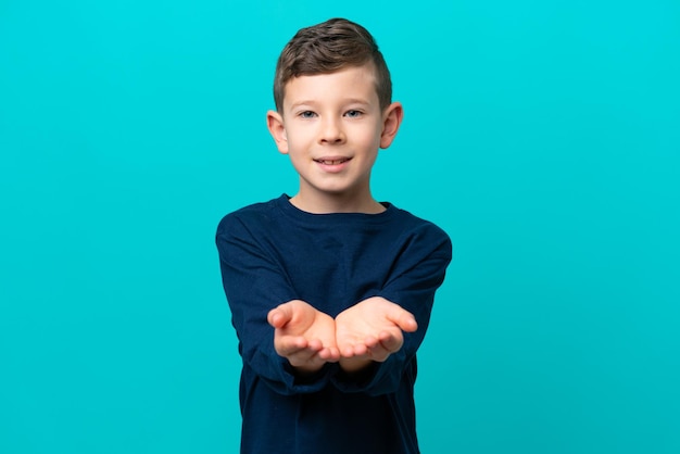 Mały chłopiec na białym tle na niebieskim tle trzymający wyimaginowaną copyspace na dłoni, aby wstawić reklamę