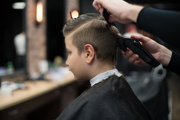 Mały chłopiec na fryzurę w fryzjera siedzi na krześle.
