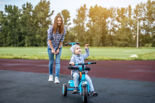 Mały chłopiec na spacerze z matką uczy się jeździć na trójkołowym dziecięcym rowerze