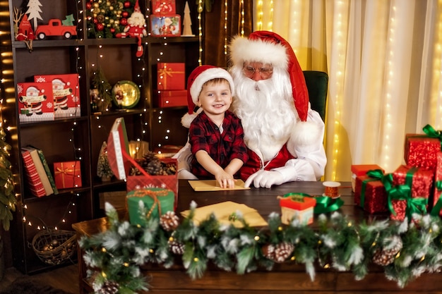 Mały chłopiec odwiedza Świętego Mikołaja, pomaga mu otworzyć koperty z świątecznymi listami koncepcja wakacji