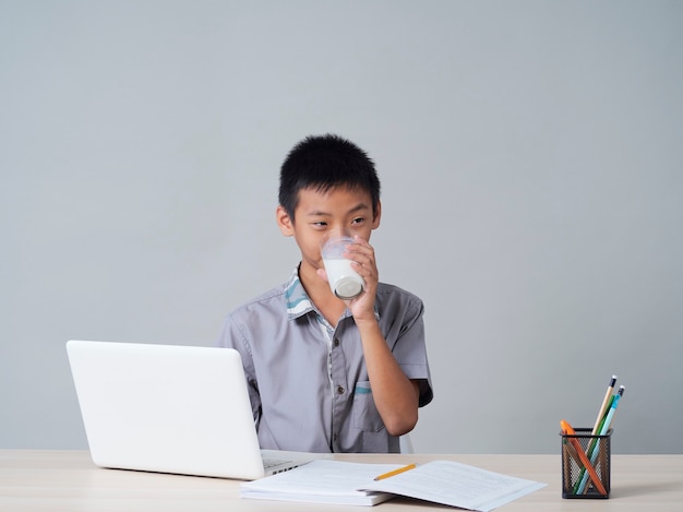 Mały chłopiec pije mleko podczas nauki online w domu