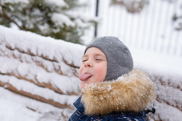 Zdjęcie mały chłopiec próbuje łapać płatki śniegu językiem zimą na ulicy