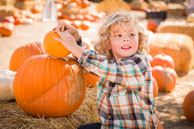 Mały chłopiec siedzący i trzymający dynię w Pumpkin PatchxA