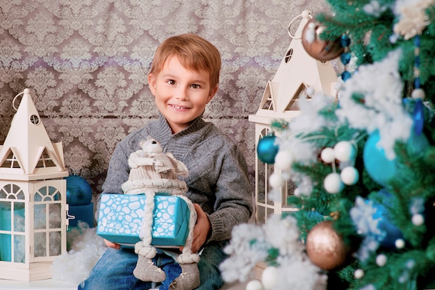 mały chłopiec siedzący z prezentem świątecznym w pobliżu choinki i ozdób choinkowych