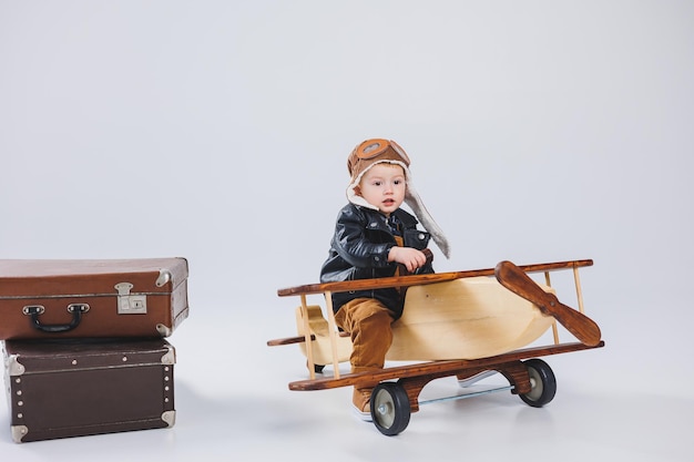 Mały chłopiec siedzi na drewnianym samolocie Ekologiczne zabawki dla dzieci Chłopiec w skórzanej kurtce i czapce