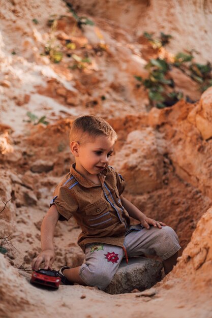 Mały chłopiec siedzi na piasku bawiąc się małym samochodem
