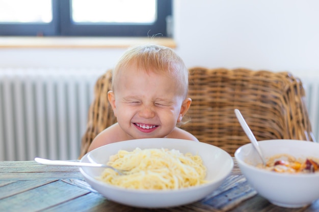 Mały chłopiec siedzi przy stole w kuchni i je spaghetti z serem. Maluch jedzący obiad. Zdrowa żywność dla koncepcji dzieci.