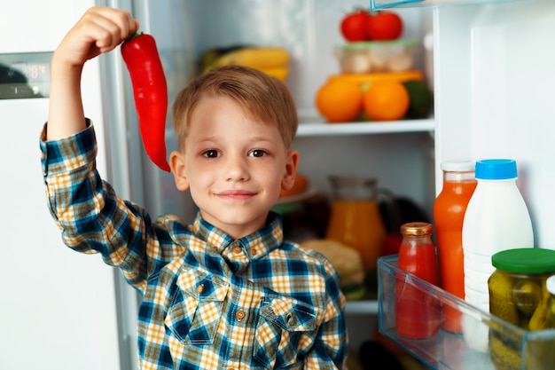 Mały chłopiec stoi przed otwartą lodówką i wybiera jedzenie