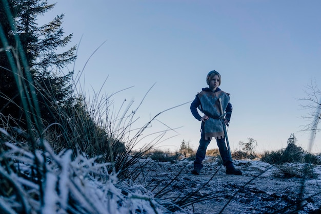Mały chłopiec stojący na wzgórzu grający w kostiumie rycerza
