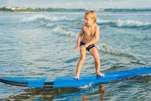 Mały chłopiec surfujący na tropikalnej plaży Dziecko na desce surfingowej na fali oceanicznej Aktywne sporty wodne dla dzieci Dziecko pływanie z surfowaniem Lekcja surfingu dla dzieci