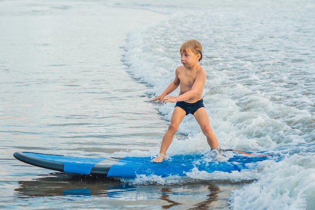 Mały chłopiec surfujący na tropikalnej plaży Dziecko na desce surfingowej na fali oceanicznej Aktywne sporty wodne dla dzieci Dziecko pływanie z surfowaniem Lekcja surfingu dla dzieci