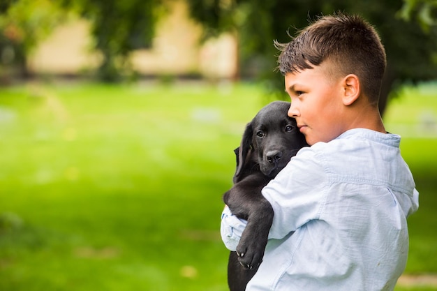 Mały chłopiec trzyma w ramionach czarnego labradora Chłopiec przytula swojego ulubionego psa na zewnątrz