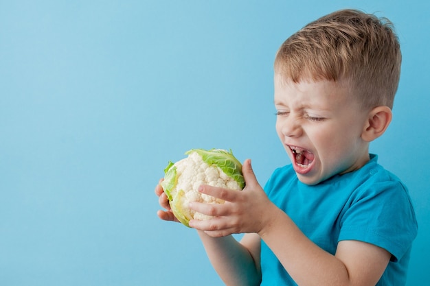 Mały chłopiec trzymający brokuły w dłoniach na niebieskim tle, dieta i ćwiczenia dla dobrego pojęcia zdrowia.