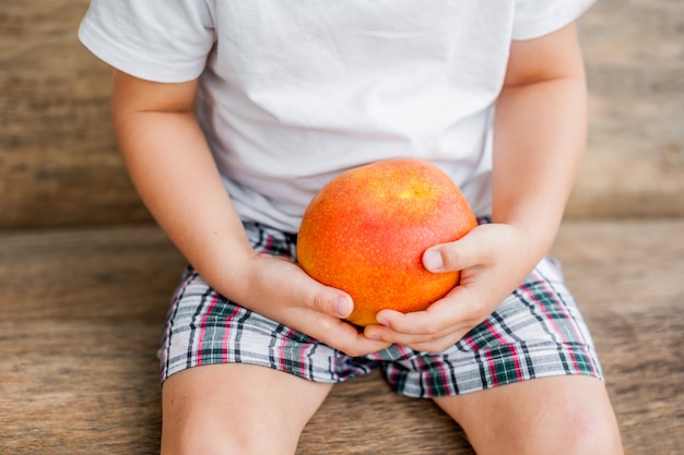 Mały chłopiec trzymający mango w dłoniach