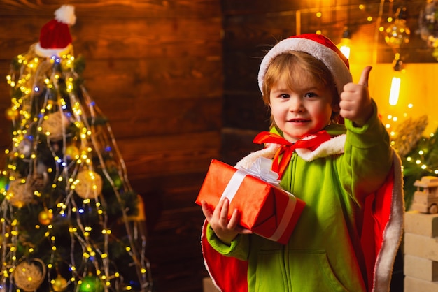 mały chłopiec ubrany w santa trzymając prezent w pomieszczeniu