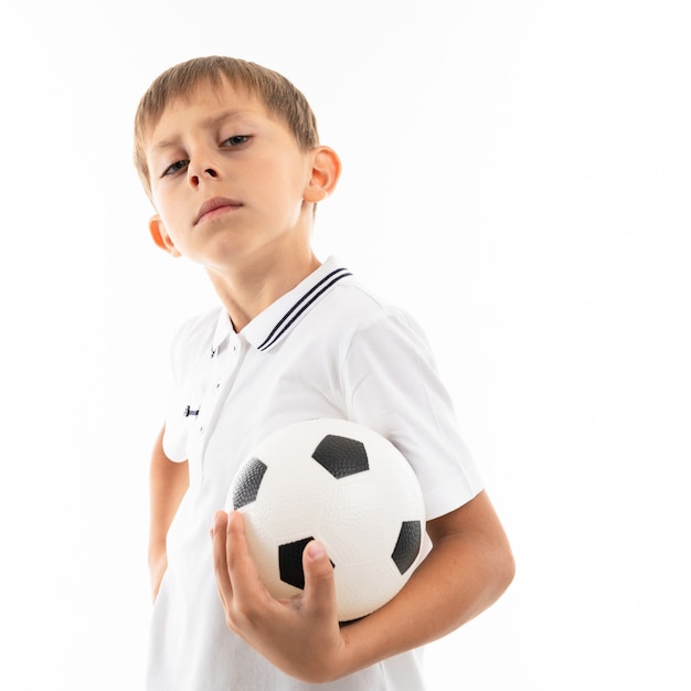 Mały chłopiec w białej koszuli, niebieskich szortach z blond włosami i piłką nożną