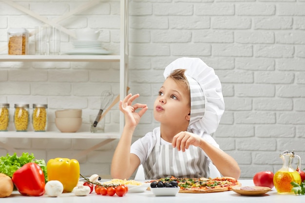 Mały chłopiec w kapeluszu szefa kuchni i fartuchu do gotowania pizzy
