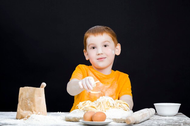 Mały chłopiec w kuchni pomagając przygotować jedzenie chłopiec z rudymi włosami i pięknymi rysami twarzy dziecko bawi się mąką w kuchni
