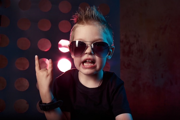 Mały chłopiec w okularach przeciwsłonecznych pokazuje palce