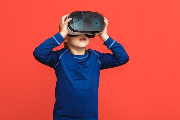 Mały chłopiec w okularach wirtualnej rzeczywistości grający w grę na czerwonym tle Technologia gadżetów 3D Kartonowe okulary do gogli VR