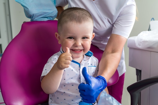 Mały chłopiec w stomatologii, uśmiechając się i pokazując kciuk do góry