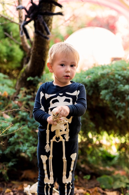 Mały chłopiec w stroju szkieletu trzymającego szkielet na imprezie z okazji halloween w ogrodzie