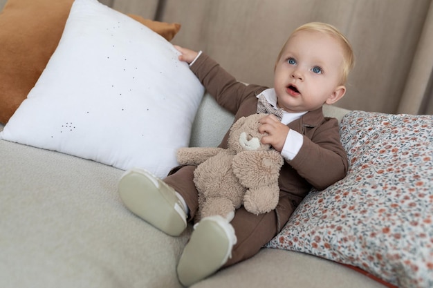 Mały chłopiec w stylowych biznesowych ubraniach z zabawką siedzi na miękkiej sofie