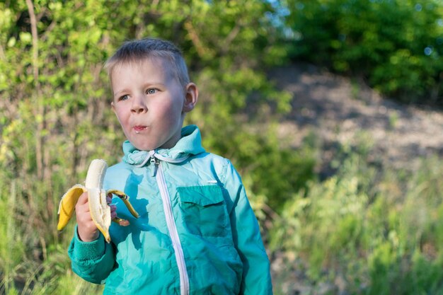 Mały chłopiec w wieku 35 lat je banana w naturze Przekąska podczas spaceru na świeżym powietrzu