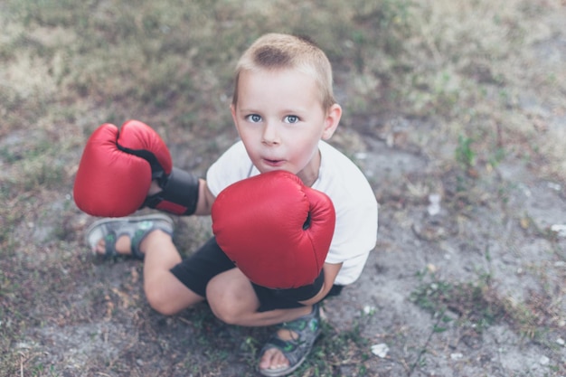 Mały chłopiec w wieku 45 lat w czerwonych rękawicach bokserskich na ulicy