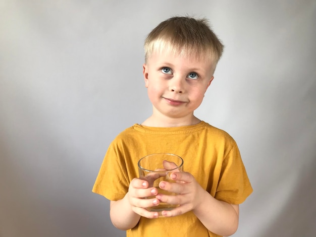 mały chłopiec w żółtej koszulce pije wodę