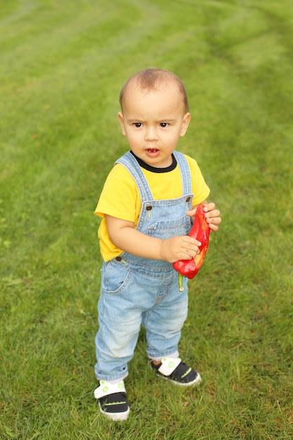 mały chłopiec w żółtej koszulce stoi na trawniku w parku trzymając czerwoną paprykę