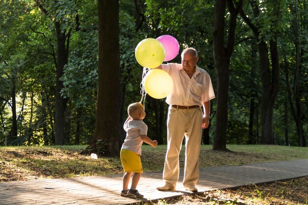 Mały chłopiec w żółtych spodenkach i starszy staruszek bawią się jasnymi balonami, którymi jest rodzina