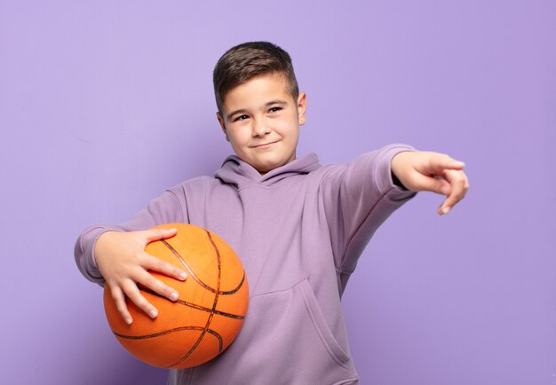 Mały chłopiec wskazujący lub pokazujący i trzymający piłkę do koszykówki